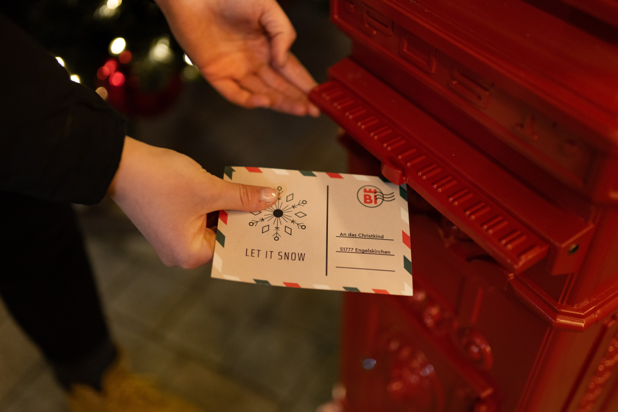 Hände werfen einen Brief ans Christkind in einen roten Briefkasten
