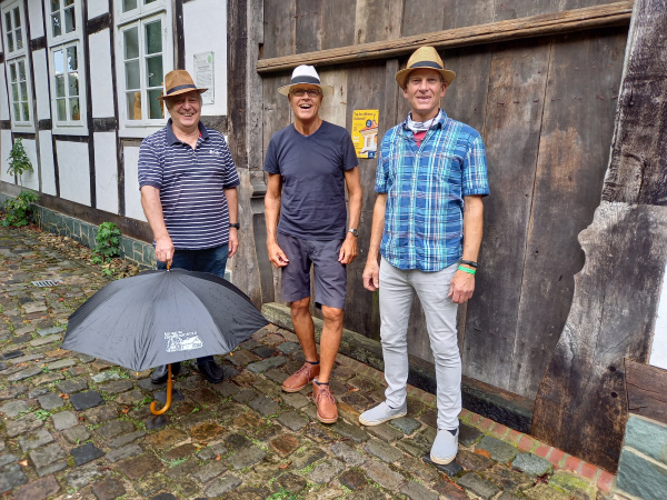 Drei Musiker mit Hut stehen vor dem Deelentor des Fachwerkhauses