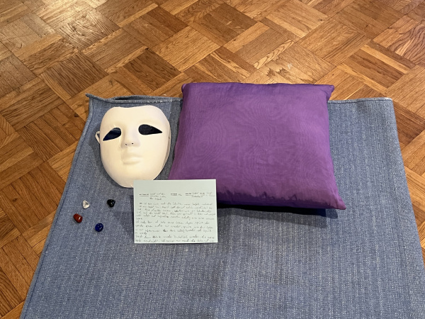 eine Decke, auf der eine weiße Maske, eine blaue Karte, ein lilafarbenes Kissen & Edelsteine liegen