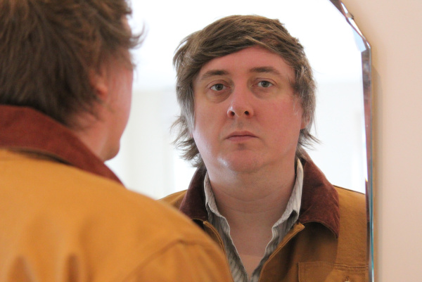 Der Sänger schaut durch einen Spiegel in die Kamera.