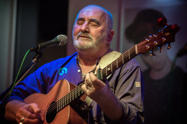 Der Sänger steht mit Akustikgitarre auf einer Bühne vor dem Mikrofon.