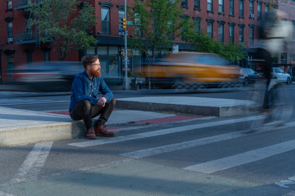 Der Sänger sitzt auf dem Bordstein am Straßenrand an einem Zebrastreifen.