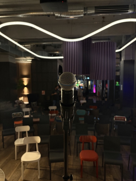 Mikrofonständer auf Bühne vor leeren Stühlen im Coworking Space bei "Heins arbeitet".