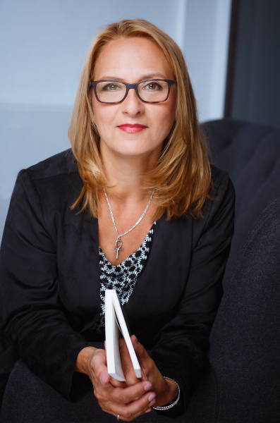 Portraitfoto der Autorin in dunkler Jacke mit Buch in den Händen vor hellem Hintergrund